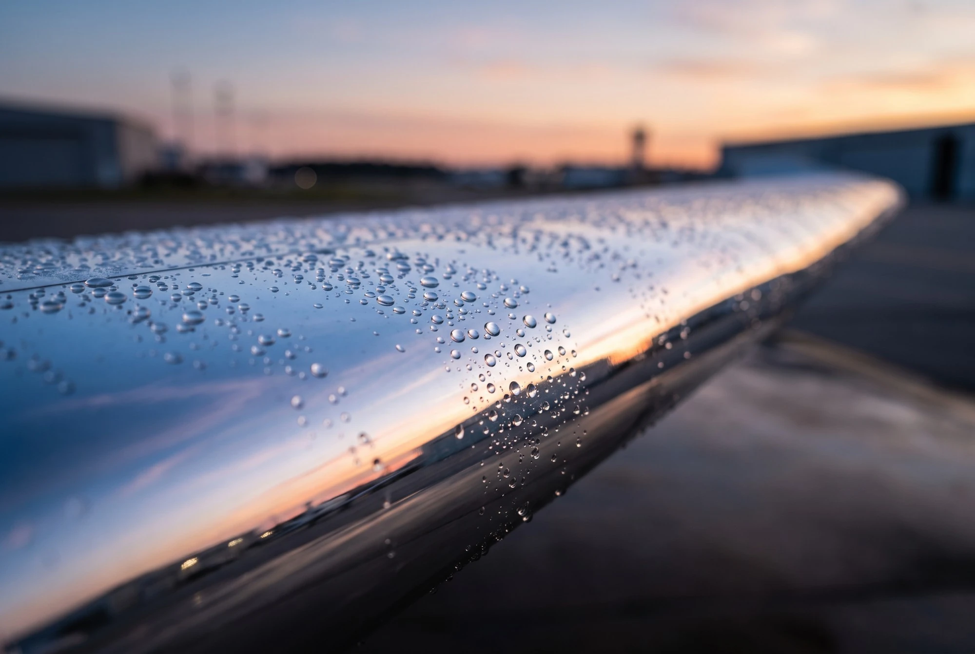 Illustration: a close-up of a polished wing edge covered in water drops, reflecting a sunset over the ramp