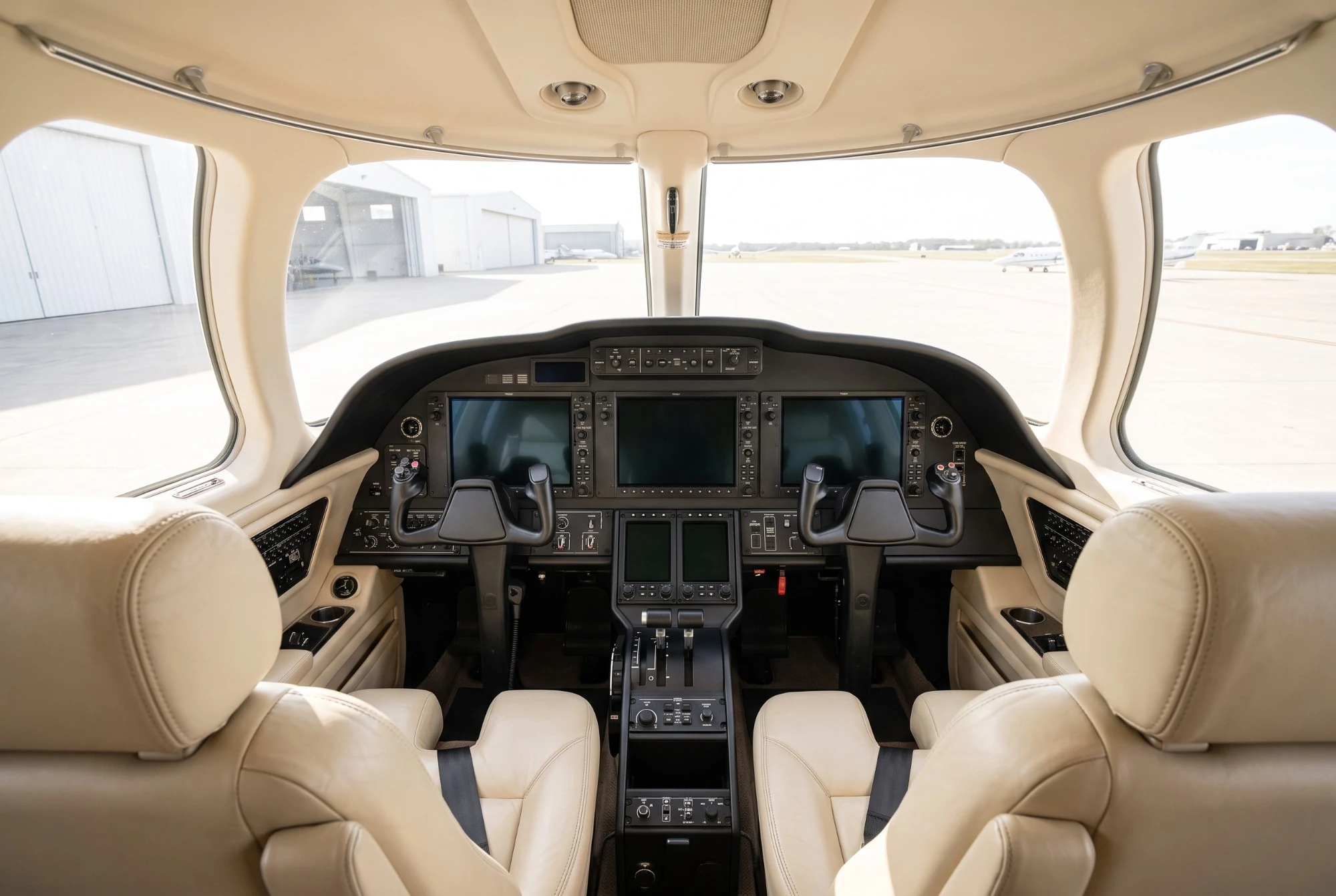Illustration: a business jet cockpit with cream leather seats, dark screens and clear windows onto the ramp