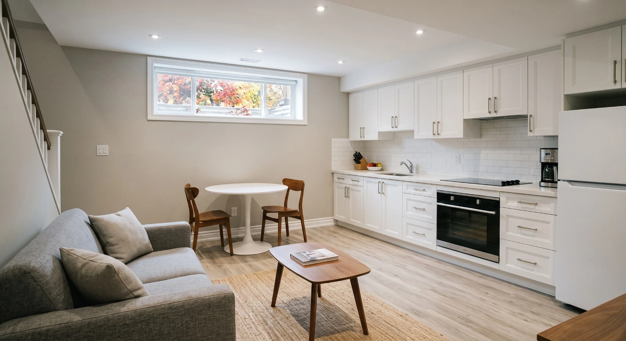 Illustration: a furnished basement suite with a white kitchen, a small round table and a sofa